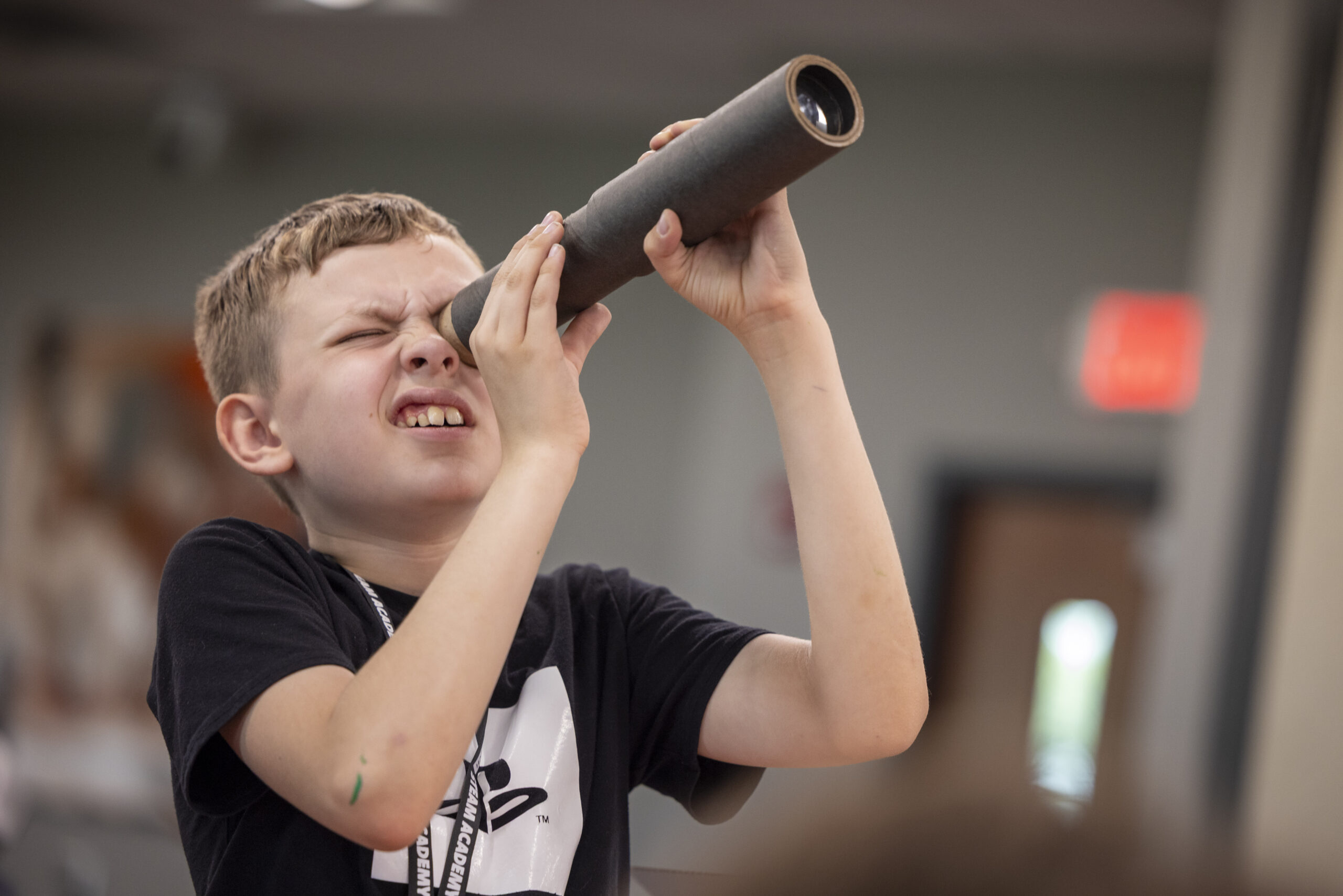 A child peers through a homemade telescope with an expression of intense focus.