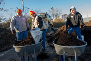 Three staff members prepping two wheelbarrows of soil