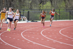 Indiana Tech relay team passing a baton in a race on the outdoor track