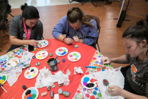 Three students sitting at a table painting their hope rocks