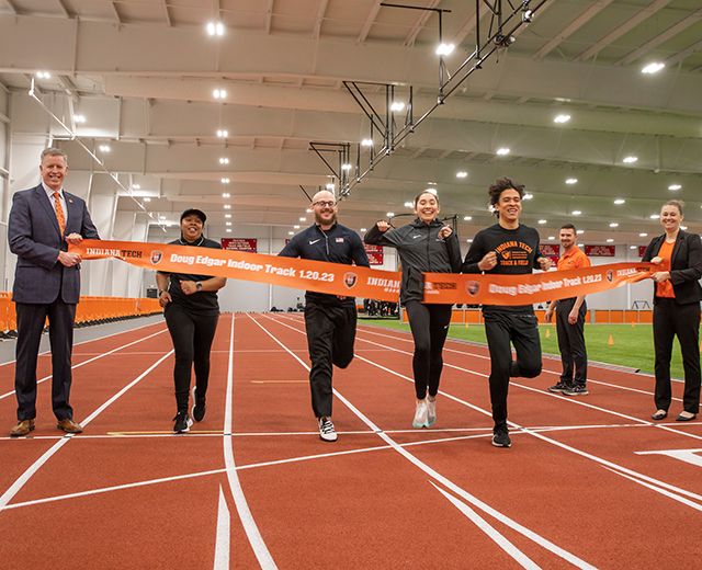 a group of indiana tech track athletes run through a ribbon at the ribbon cutting for the Doug Edgar Indoor Track